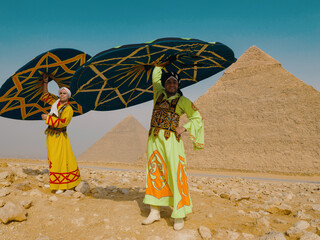 Fototapeta premium Two joyful Egyptian tanoura folk dancers spinning colorful decorated skirts overhead in bright desert sunlight before the Giza pyramids ideal for