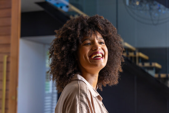 African American woman smiling and looking up while standing inside modern foyer near wooden steps