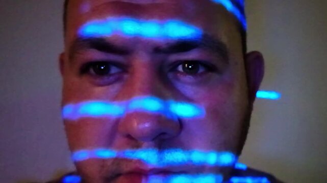Computer hacker working in dark room with blue programming code projected on his face, cyber security concept