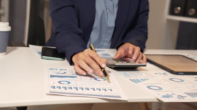 Business professional reviewing charts at a desk with tablet and calculator, showing finance analysis, budgeting, accounting, and office planning work.