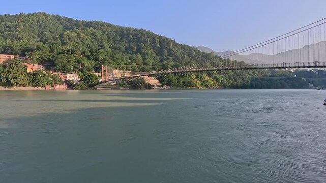 Wide-angle view of the iconic Ram Jhula suspension bridge over the Ganges River in Rishikesh, India.