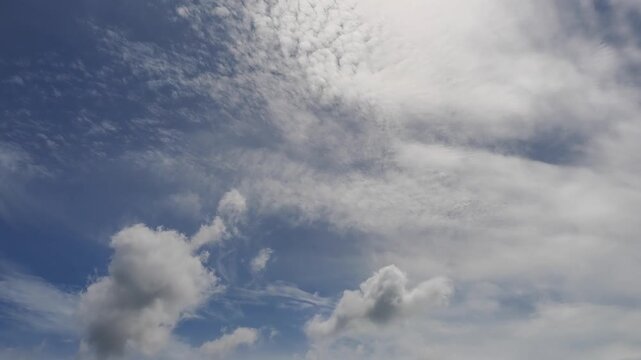 Cirrus and altocumulus clouds appear against a bright blue sky while some are thin others form denser, more puffy clusters Such cloud formations are typically associated with clear sunny weather.