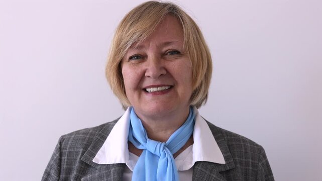 Smiling mature woman in business attire looking at camera against a plain background. Professional portrait with a friendly and confident expression.