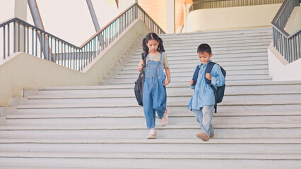 Asian children walking down school stairs with backpacks, representing education, childhood, learning journey, friendship, and daily student lifestyle. © Smile Studio AP