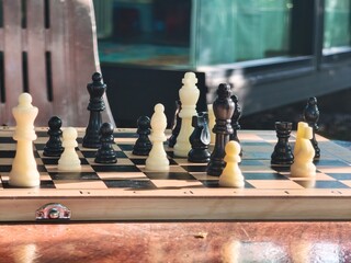 A close-up shot of a chess game in progress on a wooden board under warm sunlight, casting long shadows © Housewife Stocker