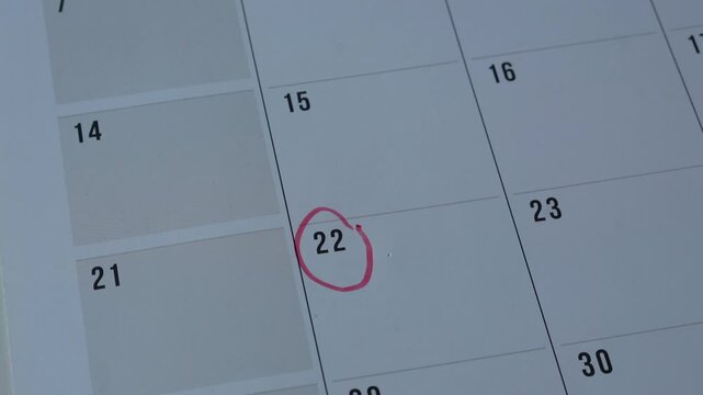 Female hand using a red marker to circle a date on a desk calendar or planner. Appointment or event planning or reminder concept