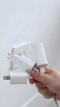 close up hand plugging adapter charge the battery with outlet socket plug and hold mobile phone on wall ,electric safety concept