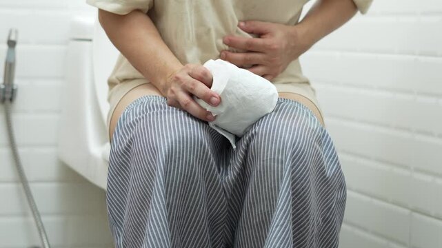 portrait of a man suffers from diarrhea his stomach painful. ache and problem. hand hold tissue paper roll in front of toilet bowl. constipation in bathroom. Hygiene, health care concept.