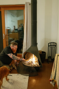 Bearded man with tattoos stokes a cozy fireplace