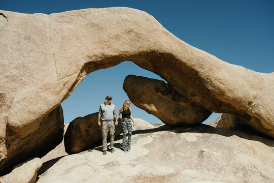 A couple holding hands under a desert rock arch