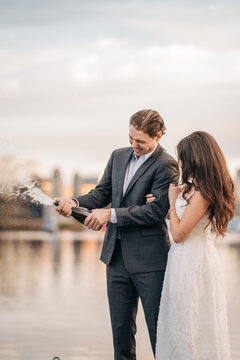 Happy couple celebrating engagement by popping champagne bottle