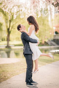 Man lifting happy woman under blooming spring trees