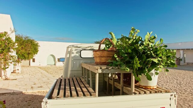 Typical white three-wheeled truck parked in the sandy courtyard of a southern italian farmhouse, carrying a potted plant and basket