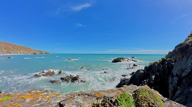 Timelapse beaches Ireland Copper Coast Waterford foaming surf yellow lichens and seapinks on rock moving clouds in blue sky summer vista