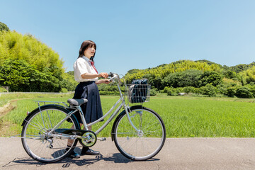 Obraz premium 田園風景の中で自転車と立つ女子高校生の通学風景