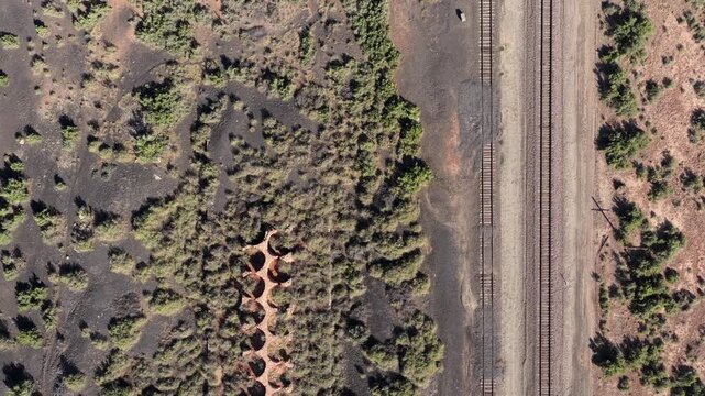 4K UHD drone footage flying over the remains of early American industrial expansion. A crumbling array of circular stone ovens sits empty among green scrub and dark stained earth.
