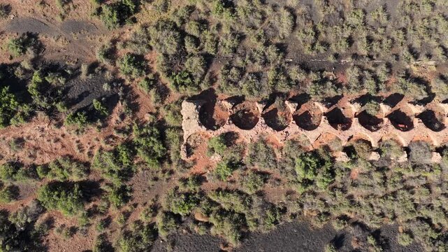 4K UHD overhead drone view looking down at a decaying line of circular coal ovens. The abandoned Waldo ghost town ruins are slowly being reclaimed by wild brush and dark soil.