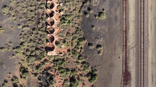 4K UHD birds-eye drone shot revealing the reddish collapsed interiors of an old coal oven line. Dark ground and wild bushes surround the forgotten circular ruins of a past era.