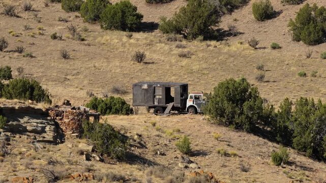 4K UHD drone video: an abandoned makeshift wooden truck dwelling rusts beside a decaying stone structure built into the hillside. This forgotten Waldo ghost town relic shows western history.