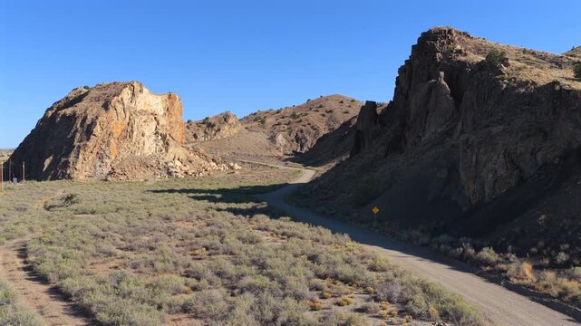 4K UHD drone reveal shot of a winding desert dirt road curving through Waldo Canyon, New Mexico. Towering rocky cliffs frame this remote southwest mountain pass landscape.