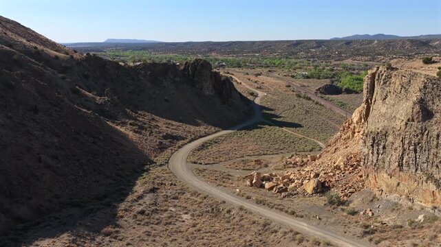 4K UHD drone video capturing a dramatic reveal of the canyon road winding through Waldo Canyon, New Mexico. Massive rock formations cast shadows across this remote southwest desert driving route.