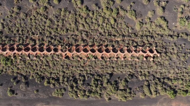 4K UHD top-down drone angle capturing a long row of deteriorating historic coal ovens. The repeating circular structures highlight forgotten mining history left behind in the dirt.