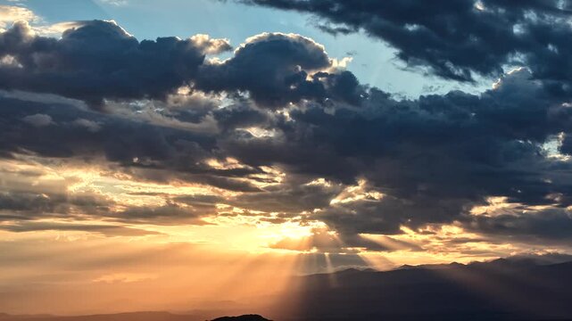 4K UHD drone timelapse: glorious radiant sunbeams burst dramatically through a heavy, dark cloud layer. The low morning sun casts breathtaking golden light rays across the distant horizon.