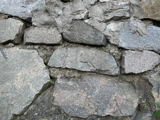 Rustic stone wall background grey granite masonry texture rough boulder rocks with cement mortar and tiny green grass sprouts © Olena Dmitriieva
