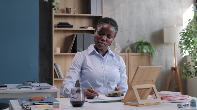 African american businesswoman writing notes at office desk