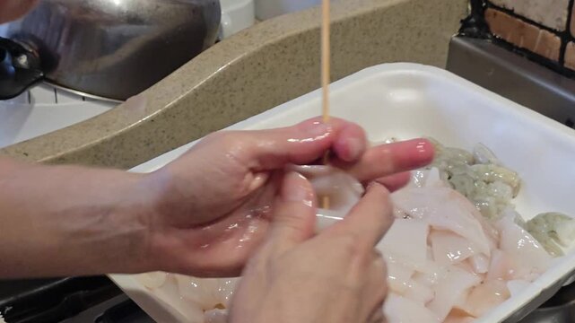 Woman hands skewering raw fresh squid on wooden stick from plastic tray preparing traditional delicious seafood skewers inside domestic kitchen in Italy cooking concept. Video 4k