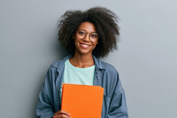 Obraz premium Young student smiling and holding an orange folder in a relaxed studio pose for education banner and social media background