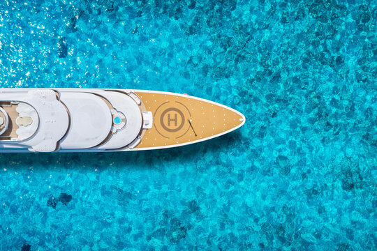 Overhead aerial view of a modern luxury cacht with wooden teak deck anchored over turquoise shining ocean with vibrant colours