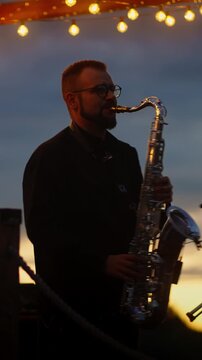 Male saxophonist performing outdoors at sunset with rimlit tenor saxophone