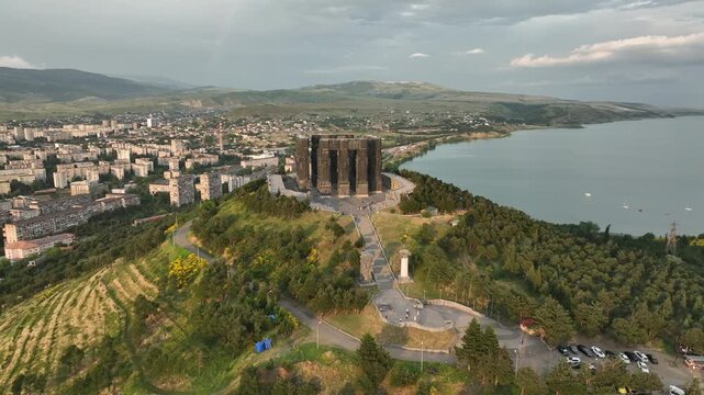 Drone shot capturing the historical Chronicle of Georgia monument complex during a scenic evening sunset. The huge stone pillars are set on a green hill next to the calm Tbilisi Sea reservoir