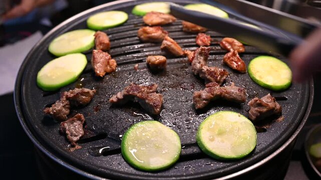 Grilling Meat and Vegetables on a Hot Plate with Tongs in a Restaurant Setting