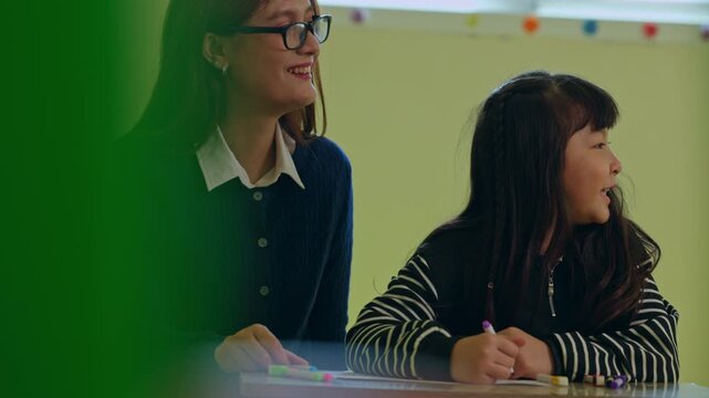 Smiling teacher guides child in classroom learning education activity with writing practice as student studies at school desk during cheerful indoor lesson