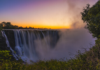 Naklejka premium Majestic Victoria Falls with golden sunset and rare lunar rainbow moon bow at night