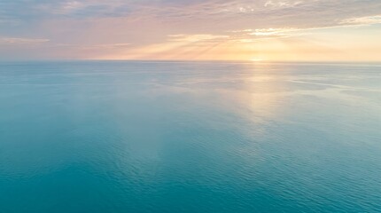 Fototapeta premium Aerial view of vast turquoise ocean stretching toward a soft sunrise horizon