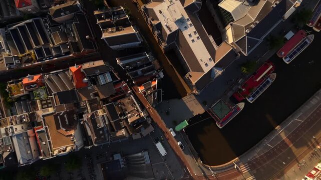 Aerial drone flies along a narrow Amsterdam canal revealing a tourist boat between rows of historic houses