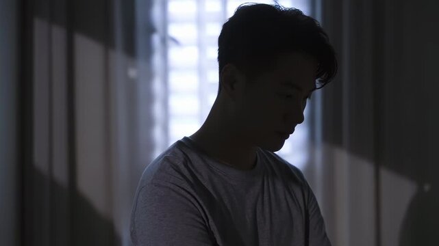 Distressed young husband man with hands on face looks worried and sad, showing stress, pain, headache, sadness, heartbreak, disappointmen, head bowed in deep thought anxiety, sorrow in dark bedroom