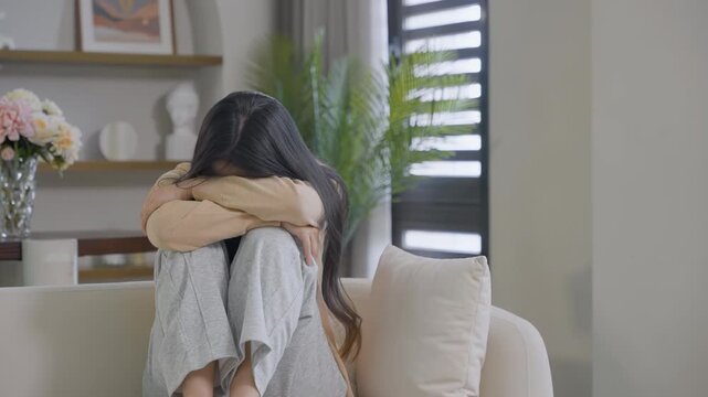 Distressed young wife woman with hands on face, curling up looks worried, crying, sad, showing stress, pain, headache, sadness, heartbreak, disappointmen, deep thought indoors anxiety, sorrow in sofa