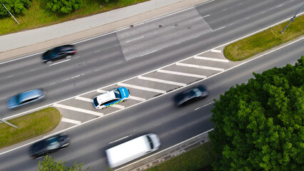 Estonian police car parked alongside a busy urban highway, monitoring speed limits and enforcing traffic regulations, with blurred vehicles indicating movement and speed © Dark Artistic