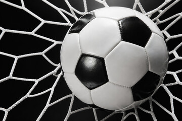 Fototapeta premium A black and white soccer ball rests inside a net against a dark background.