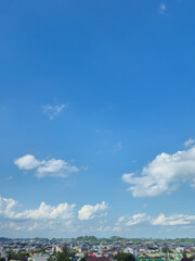 Obraz premium Blue sky with white clouds over small city landscape and green hills during daytime
