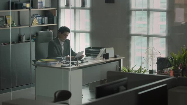A wide shot of a modern executive office with a large desk, bookshelves, and a window showing the night sky with no person present.