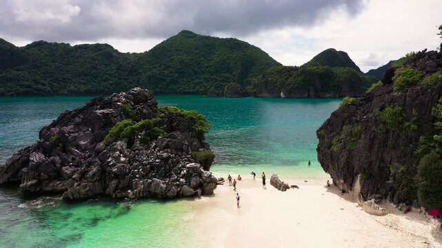 Sandy beach with tourists and tropical island by atoll with coral reef, top view. Matukad Island, Caramoan Islands, Philippines. Tourists relax on the beach.Summer and travel vacation concept