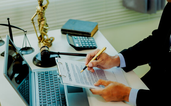 Smart corporate lawyer checking employment contract validity with Lady Justice statue on desk.