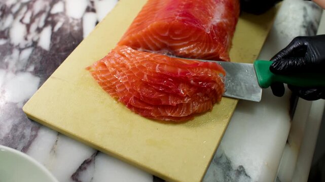 Chef fillets fresh salmon on a cutting board, removing skin with precision knife work