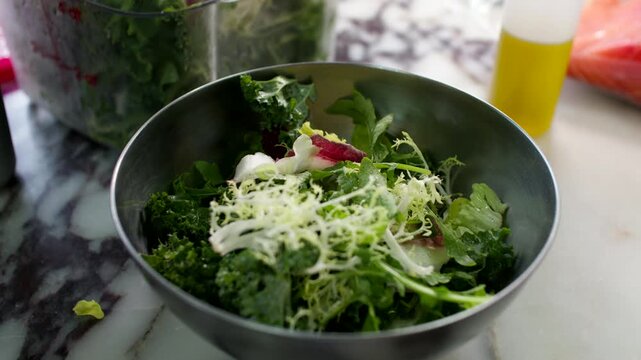 Fresh green salad with shredded cheese in metal bowl on marble kitchen counter