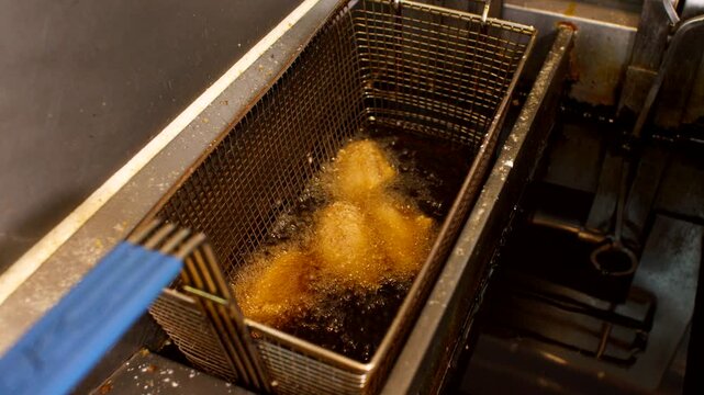 Golden battered food frying in deep fryer basket, hot oil bubbling in kitchen